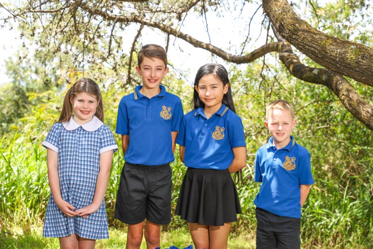 Four students in full school uniform standing infront of bushes smiling to camera