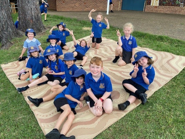 Group of students sitting together on a mat under a tree