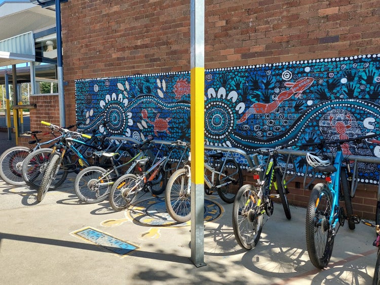 Bike rack infront of a blue Indigenous mural painted by students
