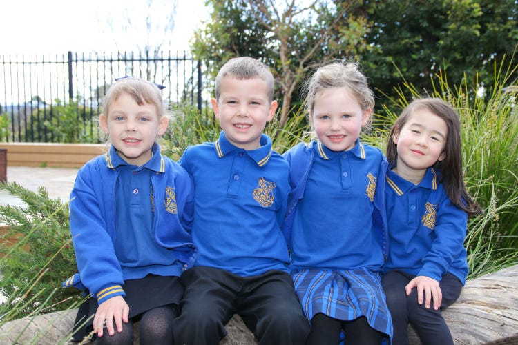 Foiur younger students smiling to camera sitting on a log in the garden