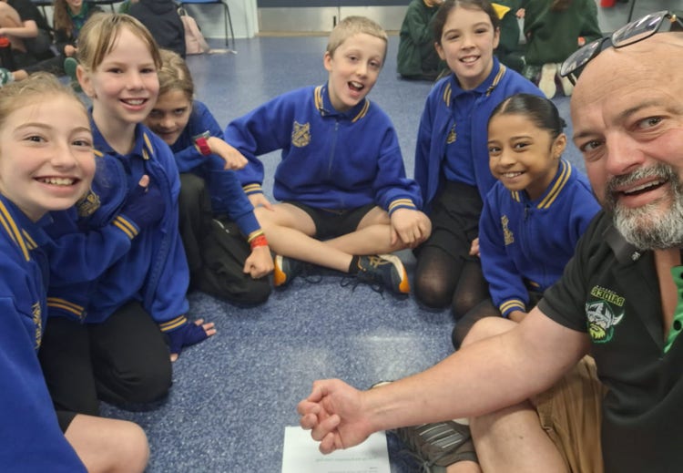 A teacher sitting on the floor with a group of students learning on ipads