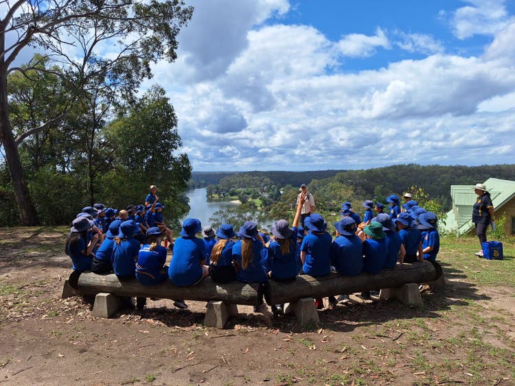A large group of students sitting on benches overlooking a river