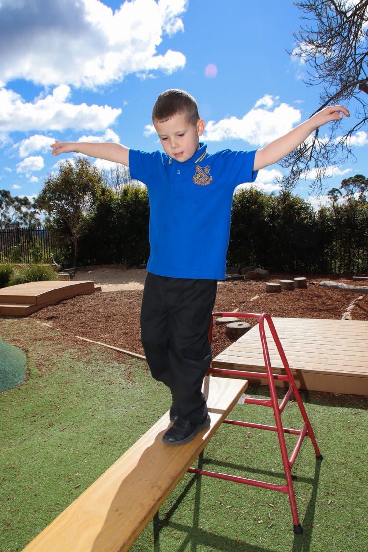 Small male student walking on a balance beam outside