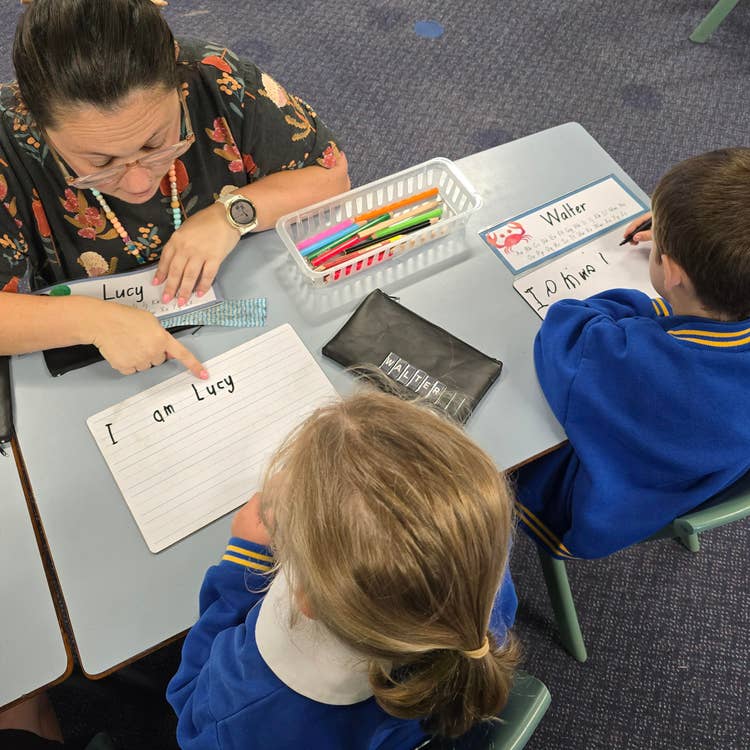 A female teacher helping two small children with their writing
