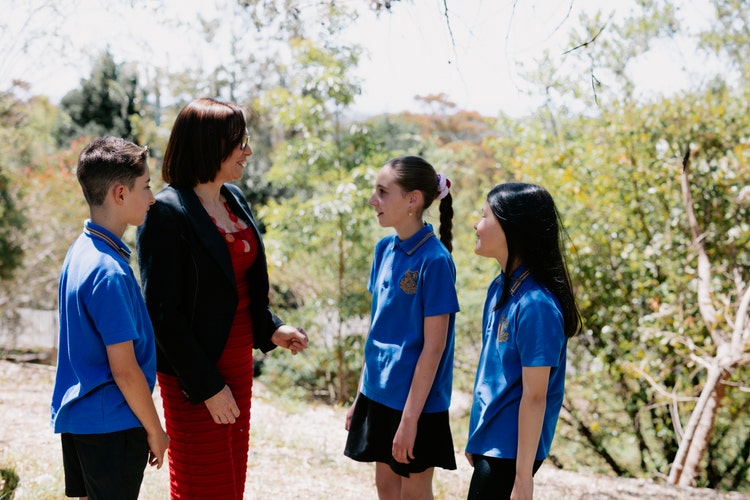 Female staff member talking to three students outdoors against bushes