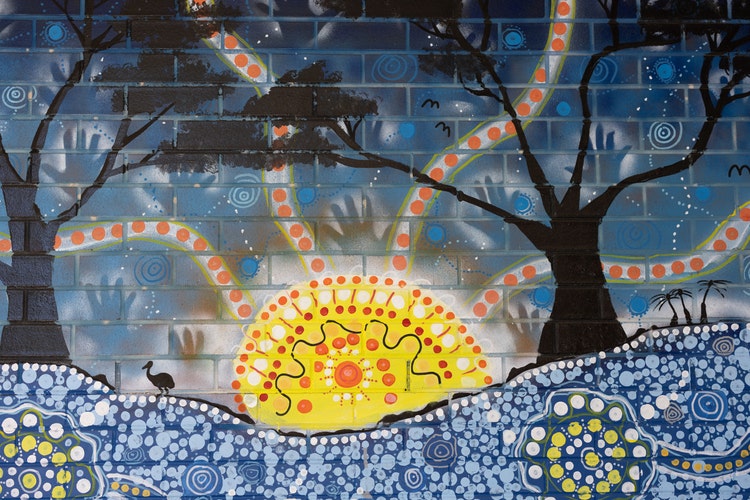 Blue Indigenous mural with a sunset painted on a brick wall