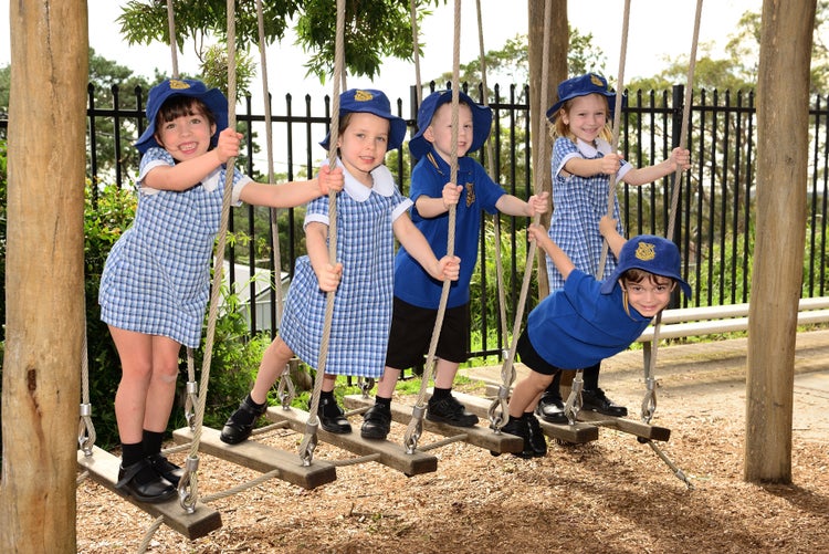 Five young students playing on a rope bridge looking to camera