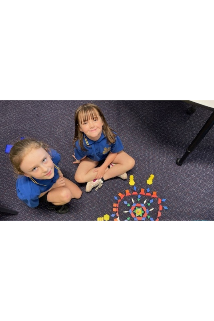 Two young female students looking up to camera with a pattern from blocka assembled on the floor.