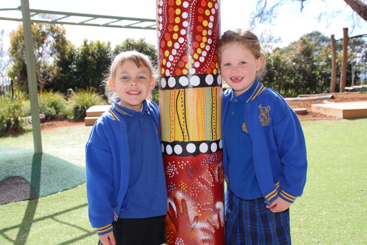 2 young femail students with their arms around a pole painted with indigenous design