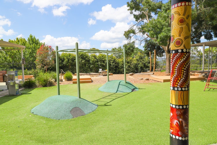 Kindergarten playground on a sunny day with climbing equipement and a pole with Indigenous painting