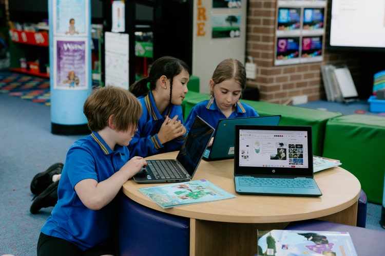 Three students sitting at a low table working on laptops