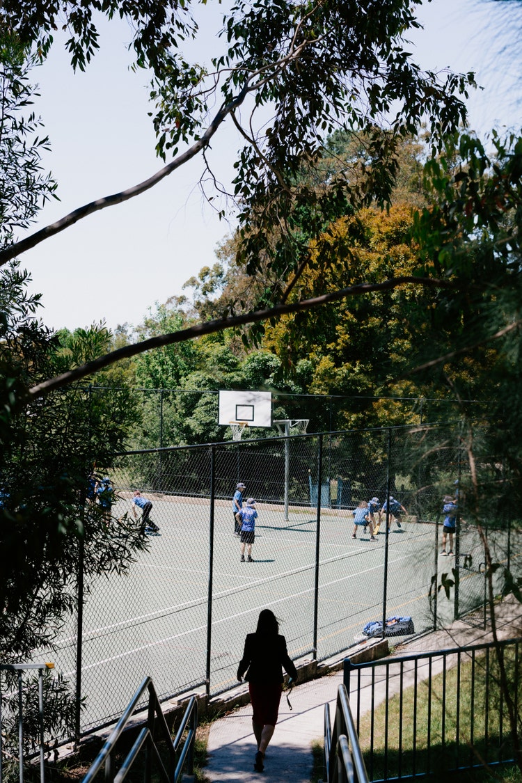 Female staff member walking down stairs towards students playing on an outdoor multi purpose court